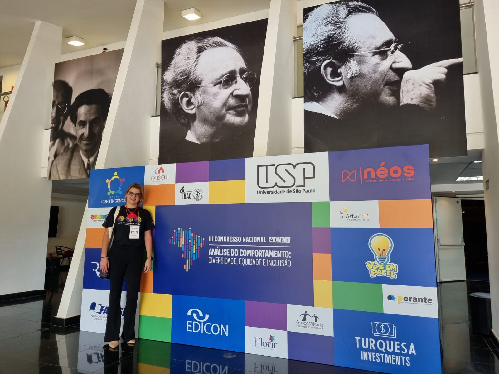 Lívia no Congresso Nacional da ACBr, com o painel de patrocinadores da USP e TatuTEA